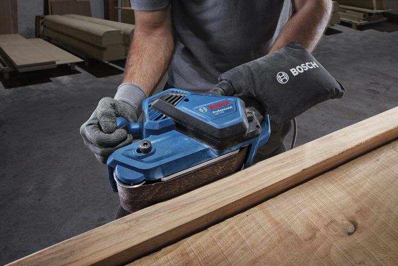 GBS 750 Person wearing safety equipment sanding wood with a blue belt sander in a workshop.