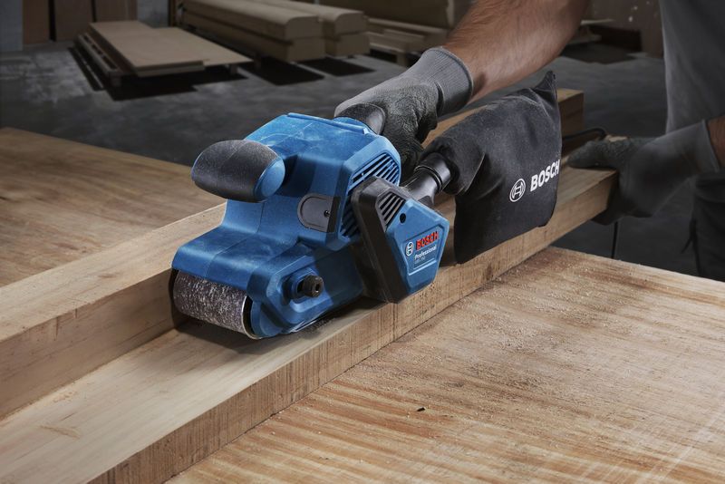 GBS 750 A person wearing safety equipment sands a wooden plank with a blue belt sander.