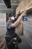 A person wearing safety equipment uses a router on a wooden shelf.