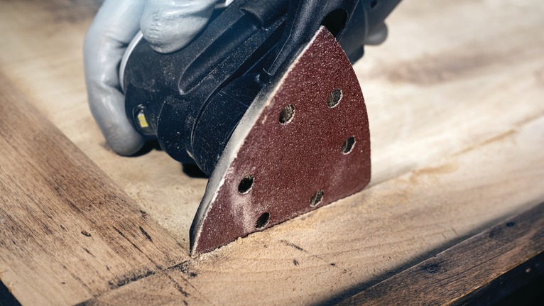 PRO F460 Sanding Sheet, 93 x 93 mm, G60, G80, G120, G180, G240, 10 pcs Person wearing safety equipment sands a wooden surface with a detail sander.