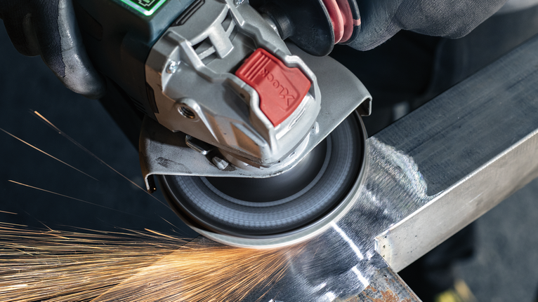 PRO R780 X-Lock Fibre Disc, 125 mm, G36 Person wearing safety equipment grinds metal, creating sparks.