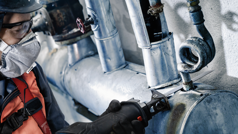 Person wearing safety equipment cuts metal piping with a power tool.
