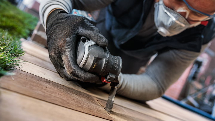Person wearing safety equipment cuts wood with a handheld power tool.