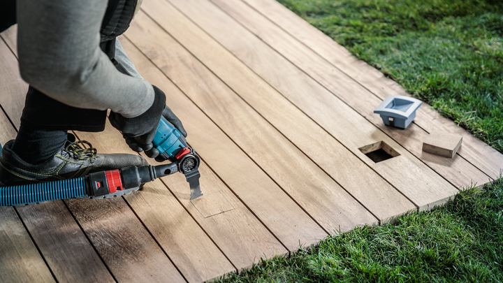 Person wearing safety equipment cuts a wooden deck with a power tool near square openings.