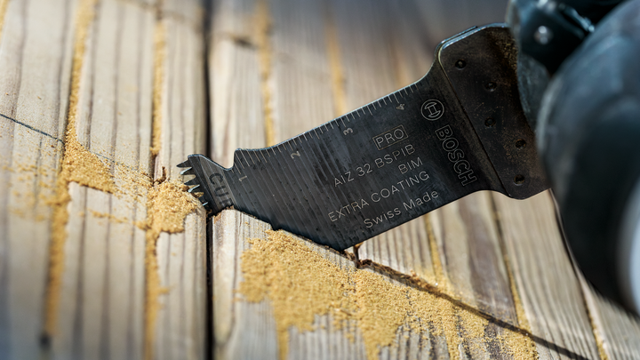 Oscillating multi-tool blade cutting grooves into wooden planks.