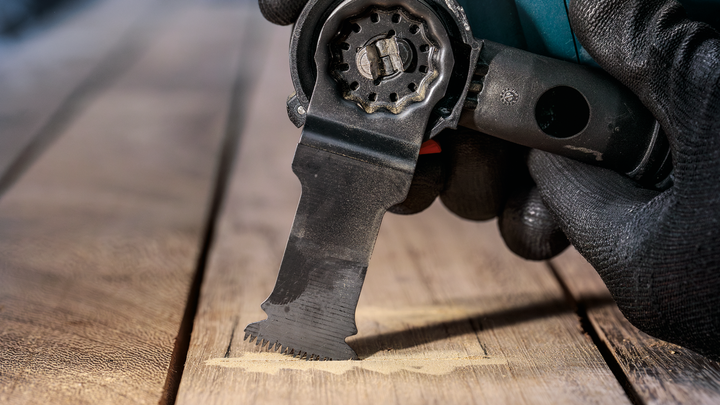 Gloved hand using an oscillating multi-tool to cut into a wooden surface.