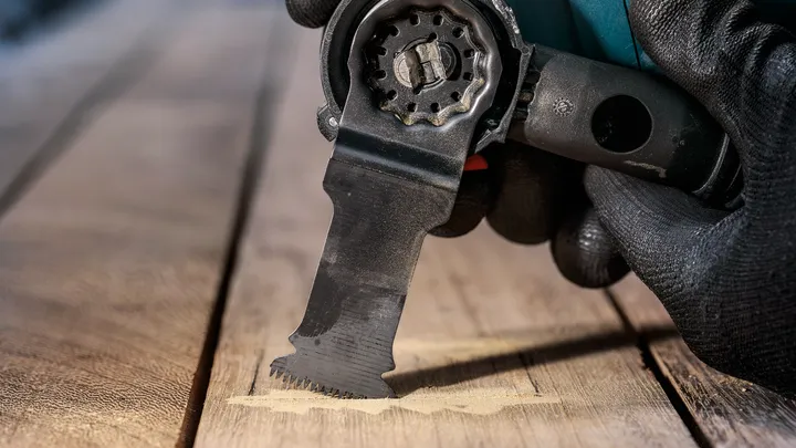 Gloved hand using an oscillating multi-tool to cut into a wooden surface.