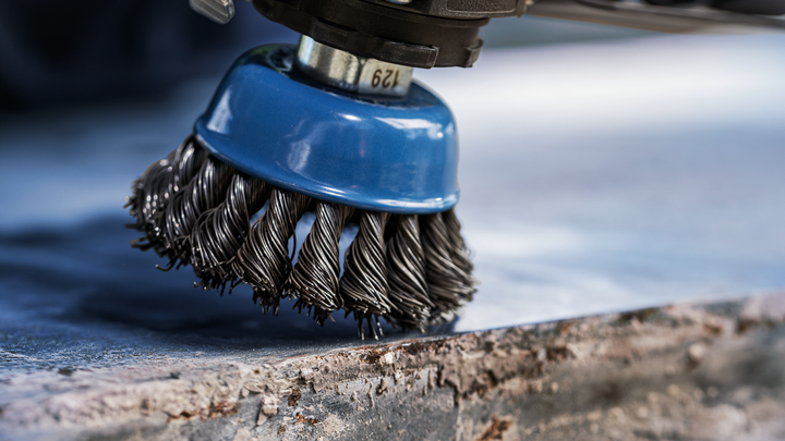 Wire brush attachment cleaning rust from the edge of a metal surface.