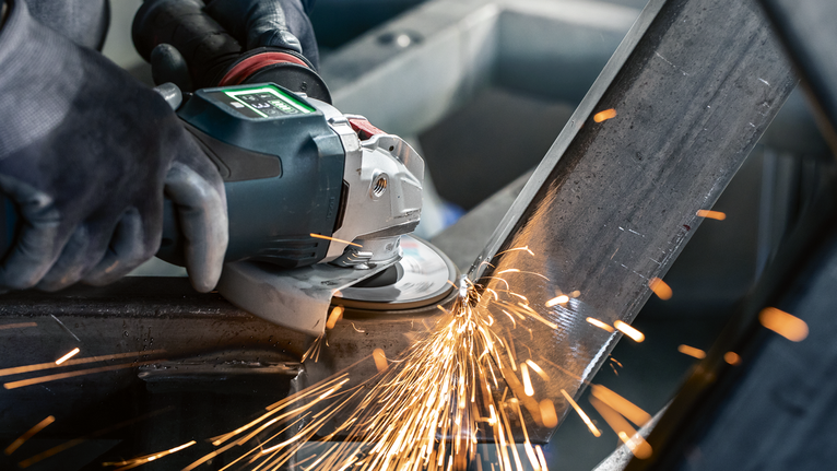 PRO X571 Flap Disc, Angled, 125 mm, G40, X-Lock A person wearing safety equipment grinds metal, producing bright sparks.