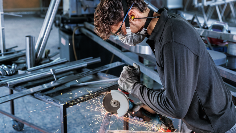 PRO Stainless Steel and Metal Bonded Cutting Disc, 115 x 1 x 22.23 mm, X-Lock, Straight Person wearing safety equipment uses an angle grinder to cut metal, producing sparks.