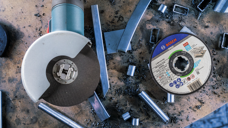 PRO Stainless Steel and Metal Bonded Cutting Disc, 115 x 1 x 22.23 mm, X-Lock, Straight Angle grinder and metal cutting disc on a workbench with scattered metal scraps.