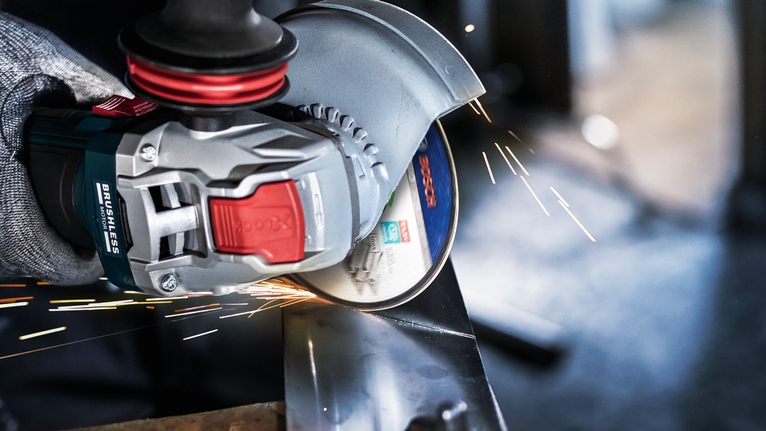 PRO Stainless Steel and Metal Bonded Cutting Disc, 115 x 1 x 22.23 mm, X-Lock, Straight A person wearing safety equipment grinds metal, creating bright sparks.