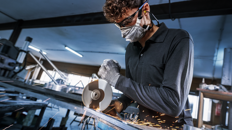 PRO Stainless Steel and Metal Bonded Cutting Disc, 115 x 1 x 22.23 mm, X-Lock, Straight Person wearing safety equipment cuts metal with an angle grinder, sparks flying.