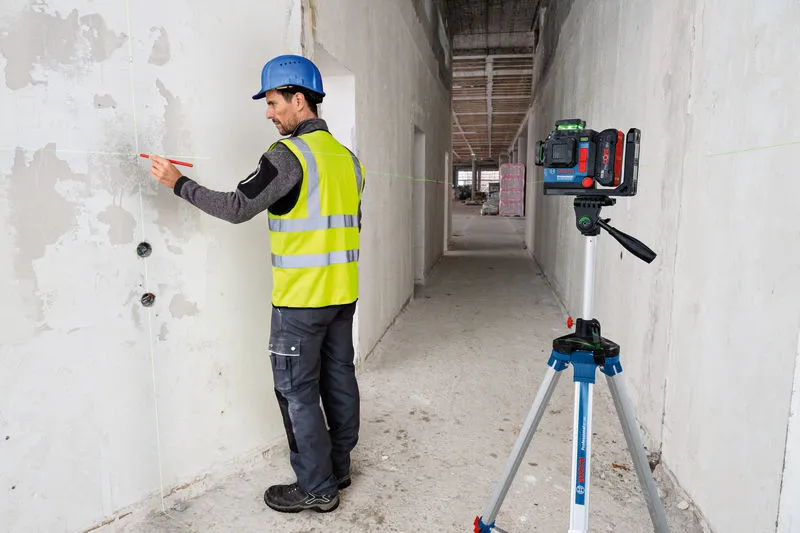 GLL 18V-120-33 CG A person wearing safety equipment marks a wall guided by a laser leveling tool on a tripod.
