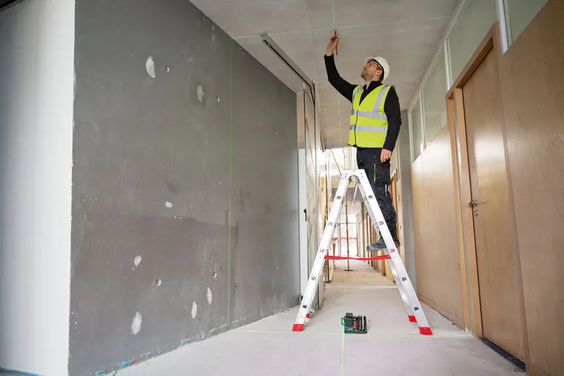 GLL 18V-120-33 CG A person wearing safety equipment marks a ceiling using a laser leveling tool.