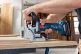 Person cuts plywood with a cordless biscuit joiner on a workbench.