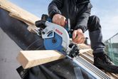 A person wearing safety equipment cuts roof timber with a cordless circular saw.
