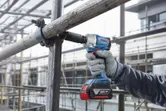 A person wearing safety equipment uses a cordless impact wrench to tighten scaffolding.