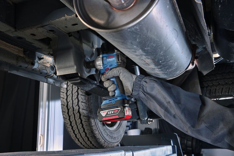 GDS 18V-350 A person wearing safety equipment tightens a bolt on a car undercarriage with a cordless impact wrench.