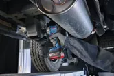 A person wearing safety equipment tightens a bolt on a car undercarriage with a cordless impact wrench.