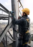 A person wearing safety equipment uses an impact wrench to fasten bolts on a metal structure.