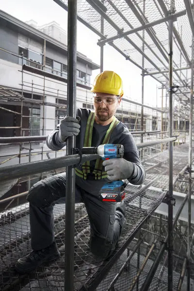 GDS 18V-350 A person wearing safety equipment tightens a pipe joint with a cordless impact wrench on scaffolding.