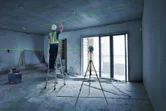 A person wearing safety equipment aligns ceiling fixtures using a laser leveling tool.
