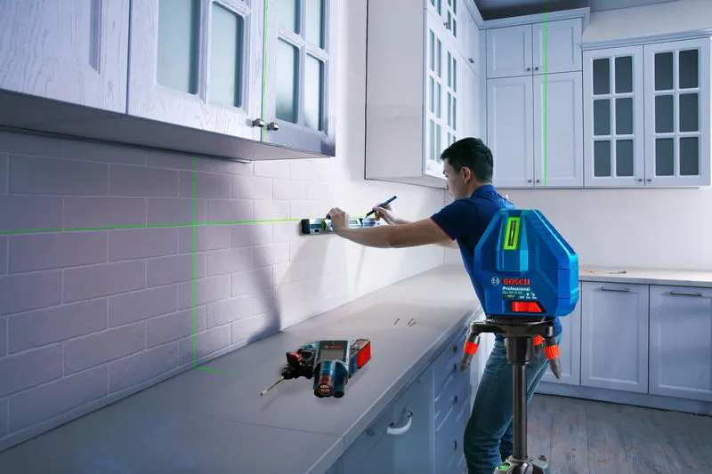 Person aligning kitchen cabinets with a laser leveling tool on a tripod.