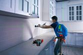 Person aligning kitchen cabinets with a laser leveling tool on a tripod.