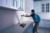 A person uses a laser leveling tool to align cabinets in a kitchen.
