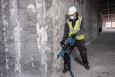 A person wearing safety equipment breaks concrete with a cordless demolition hammer.