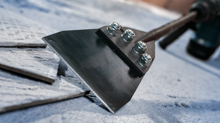 Wide chisel attachment lifting floor tiles from concrete.