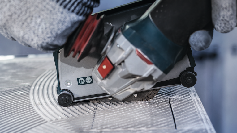 PRO Ceramic Diamond Disc, 105 x 20/16 mm Person wearing safety equipment guides a power tool to cut grooves in a tile.