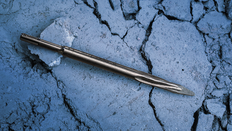 PRO SDS plus-5C Pointed Chisel, 250 mm Metal chisel bit lying on cracked concrete surface.