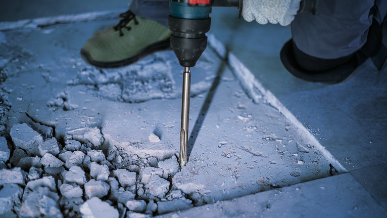 PRO SDS plus-5C Pointed Chisel, 250 mm Person wearing safety equipment uses a rotary hammer to break concrete flooring.