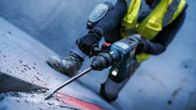 PRO SDS plus-5C Flat Chisel, 20 x 250 mm A person wearing safety equipment chisels a concrete surface with a rotary hammer.