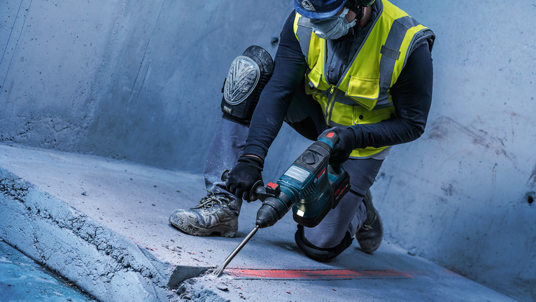 PRO SDS plus-5C Flat Chisel, 20 x 250 mm Person wearing safety equipment uses a power tool to break concrete floor.