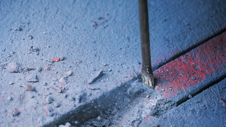 PRO SDS plus-5C Flat Chisel, 20 x 250 mm Chisel bit breaking a groove into concrete with dust scattered around.