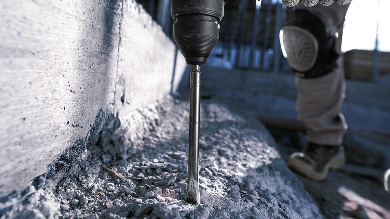 A person wearing safety equipment drills into concrete at a construction site.