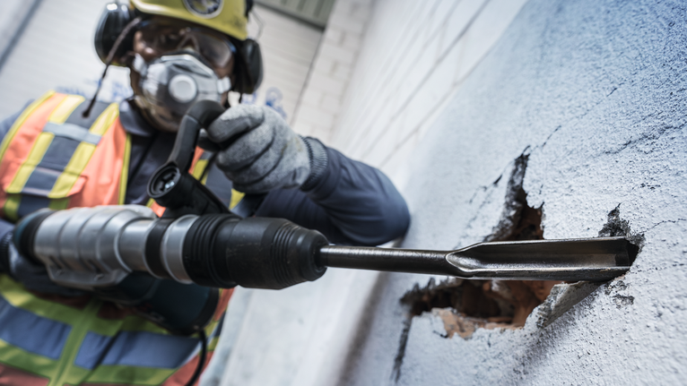 PRO SDS max Hollow Gouging Chisel, 26 x 300 mm Person wearing safety equipment uses a rotary hammer to break through a concrete wall.