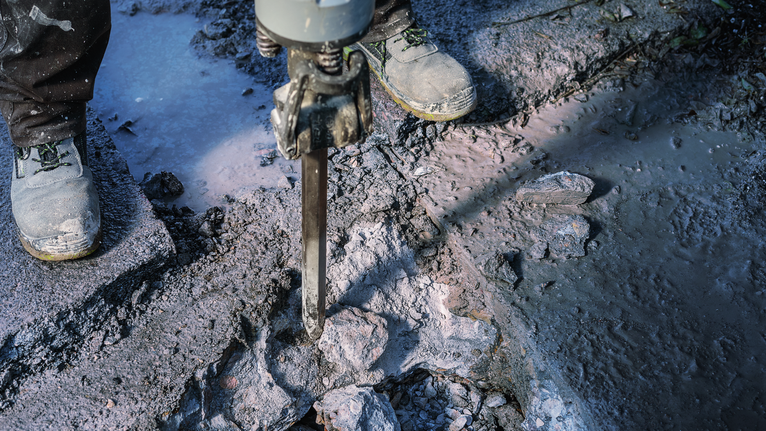 PRO HEX-4C Pointed Chisel 28 mm, 28 x 520 mm Person wearing safety equipment breaking concrete with a demolition hammer.