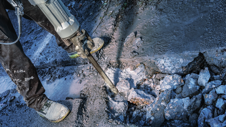 PRO HEX-4C Pointed Chisel 28 mm, 28 x 520 mm Person wearing safety equipment breaks concrete with a demolition hammer.