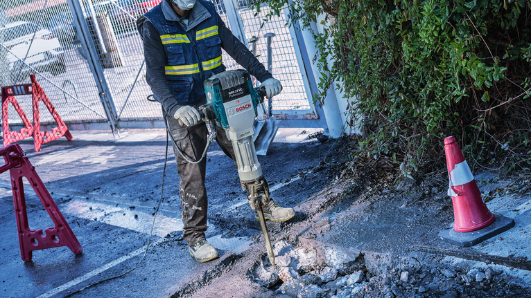 PRO HEX-4C Pointed Chisel 28 mm, 28 x 520 mm A person wearing safety equipment breaks concrete with a power demolition tool.