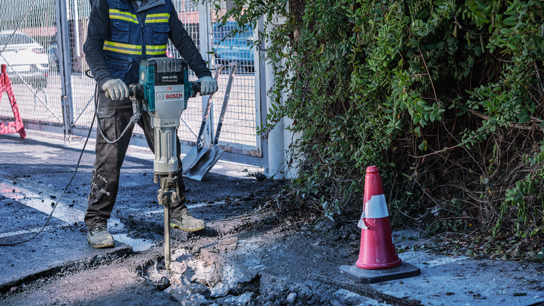 PRO HEX-4C Pointed Chisel 28 mm, 28 x 520 mm A person wearing safety equipment breaks up concrete with a demolition hammer.