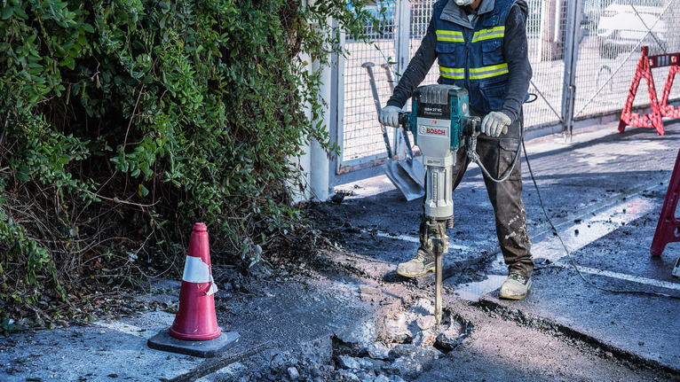 PRO HEX-4C Pointed Chisel 28 mm, 28 x 520 mm A person wearing safety equipment breaks concrete with a demolition tool.