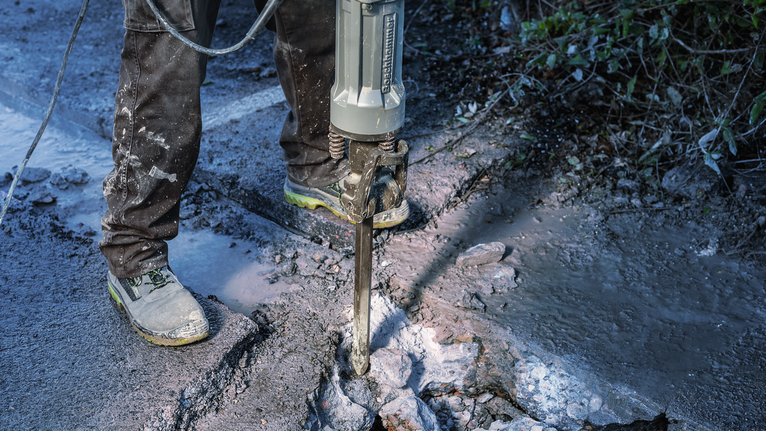 PRO HEX-4C Pointed Chisel 28 mm, 28 x 520 mm Person wearing safety equipment breaking pavement with a demolition tool.