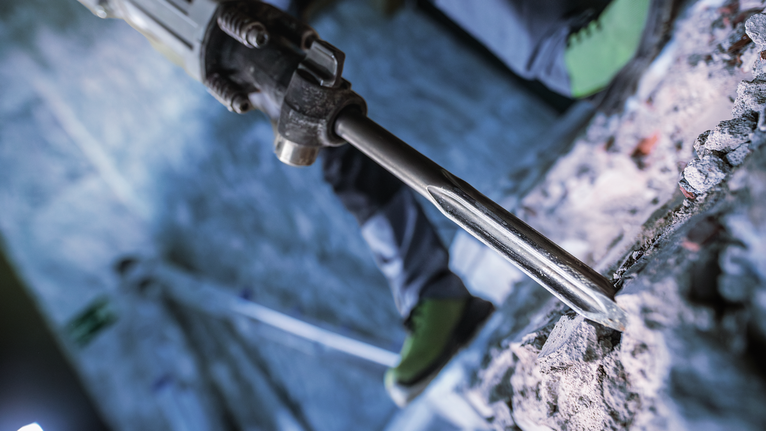 PRO HEX-5C Pointed Chisel 30 mm, 30 x 400 mm Person wearing safety equipment uses a demolition hammer to break concrete.