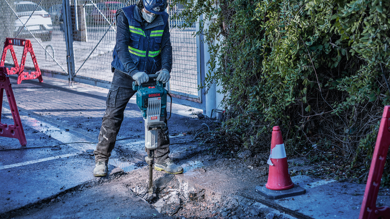 PRO HEX-4C Flat Chisel 30 mm, 35 x 400 mm A person wearing safety equipment breaks concrete with a demolition hammer on a sidewalk.