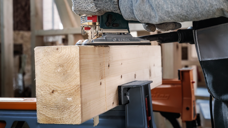 Person wearing safety equipment cutting a wooden beam with a power jigsaw.