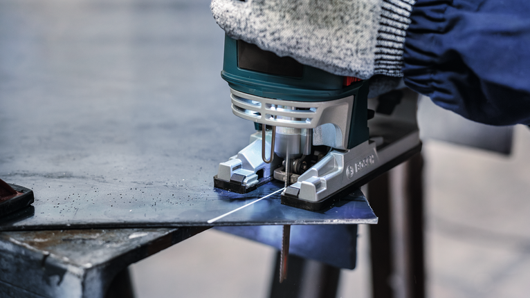 PRO Metal thick and thin T123XF Jigsaw Blade, 100 mm, 3 pcs A person wearing safety equipment cuts a sheet of metal with a jigsaw.